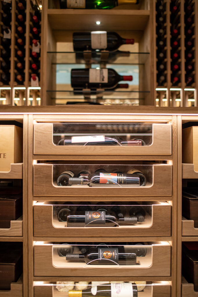 three wine cellar draws with wine bottles viewed through a glass window