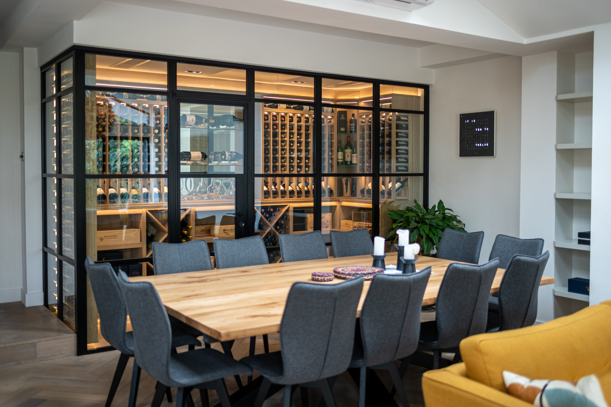 A wine cellar, central to the dining room. The wine cellar has large Crittall style doors and frame work. Through the glass, light oak wine racks can be seen, filled with wine bottles