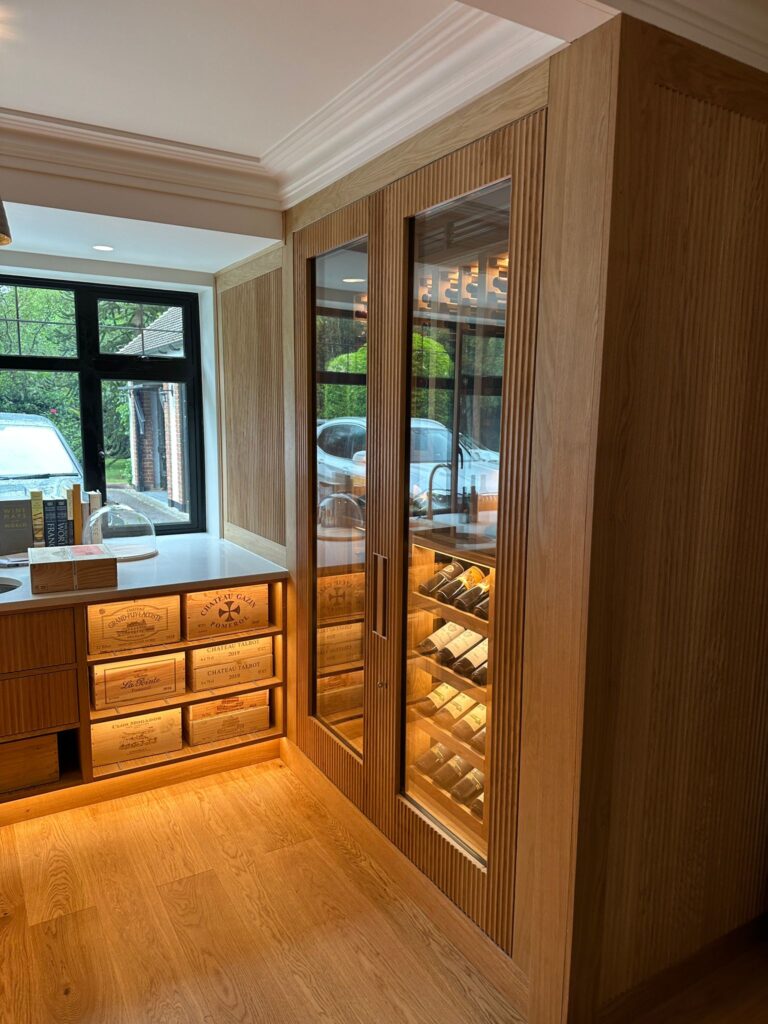 the right hand side wine wall made from light oak. The glass doors show wine bottles stored upon angled racking behind.